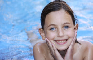 a pretty girl with blue eyes relaxing in a swimming pool smiling and looking at camera