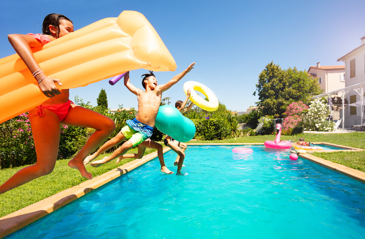 Side view portrait of teenage boys and girls with swimming tools jumping into the pool in summer