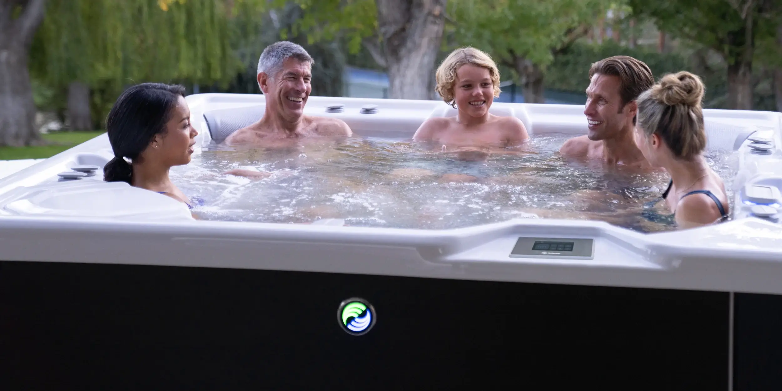 Five adults relaxing together in an alpine white Highlife&reg; spa with the jets running, on a sunlit patio
