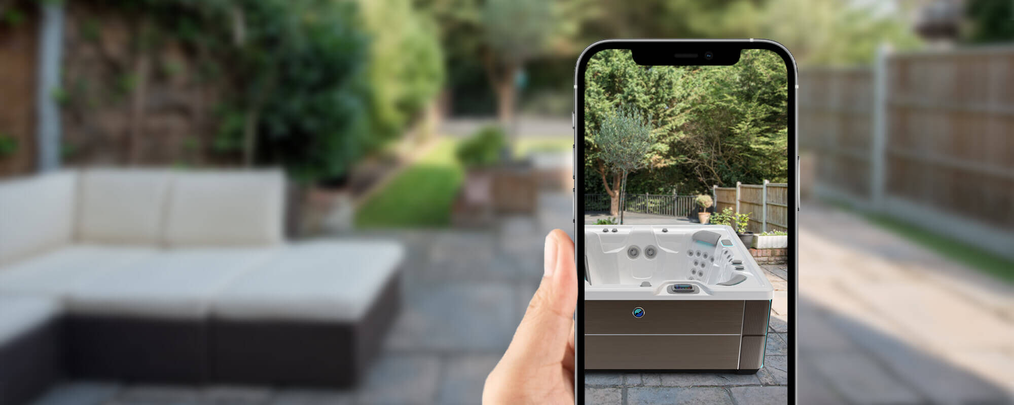 A hand holding a phone using the Hot Spring Virtual View app to preview a hot tub placed in a backyard patio